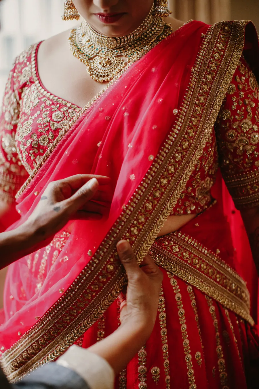 Bride in a red and gold hand-embroidered bridal lehenga being draped